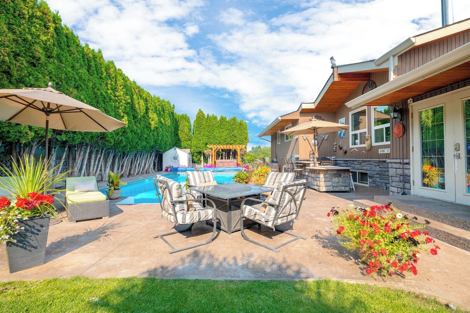Outdoor dining patio with umbrella, pool and house in the background