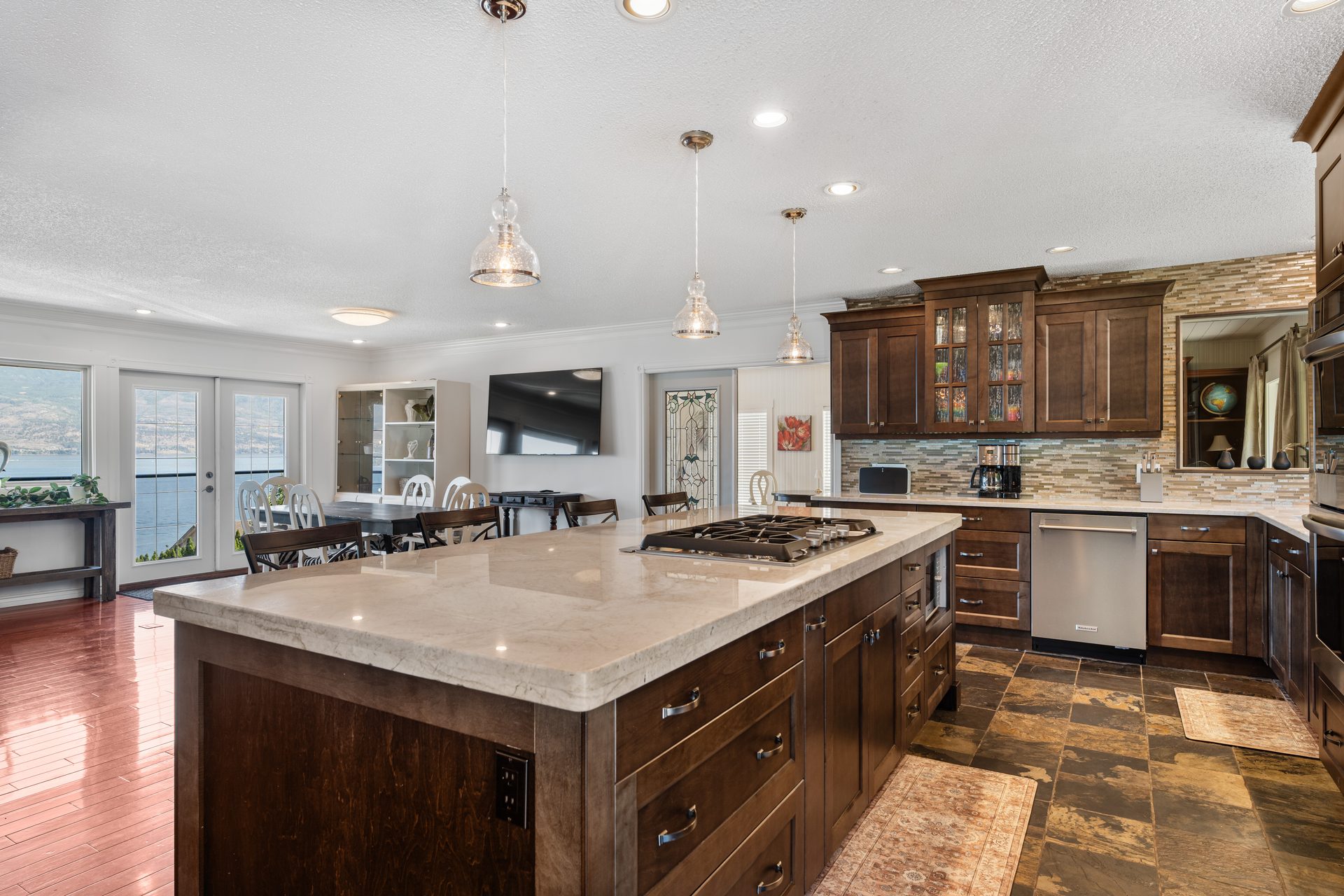 Gourmet kitchen with marble island, gas cooktop, pendant lights and lake view through dining area