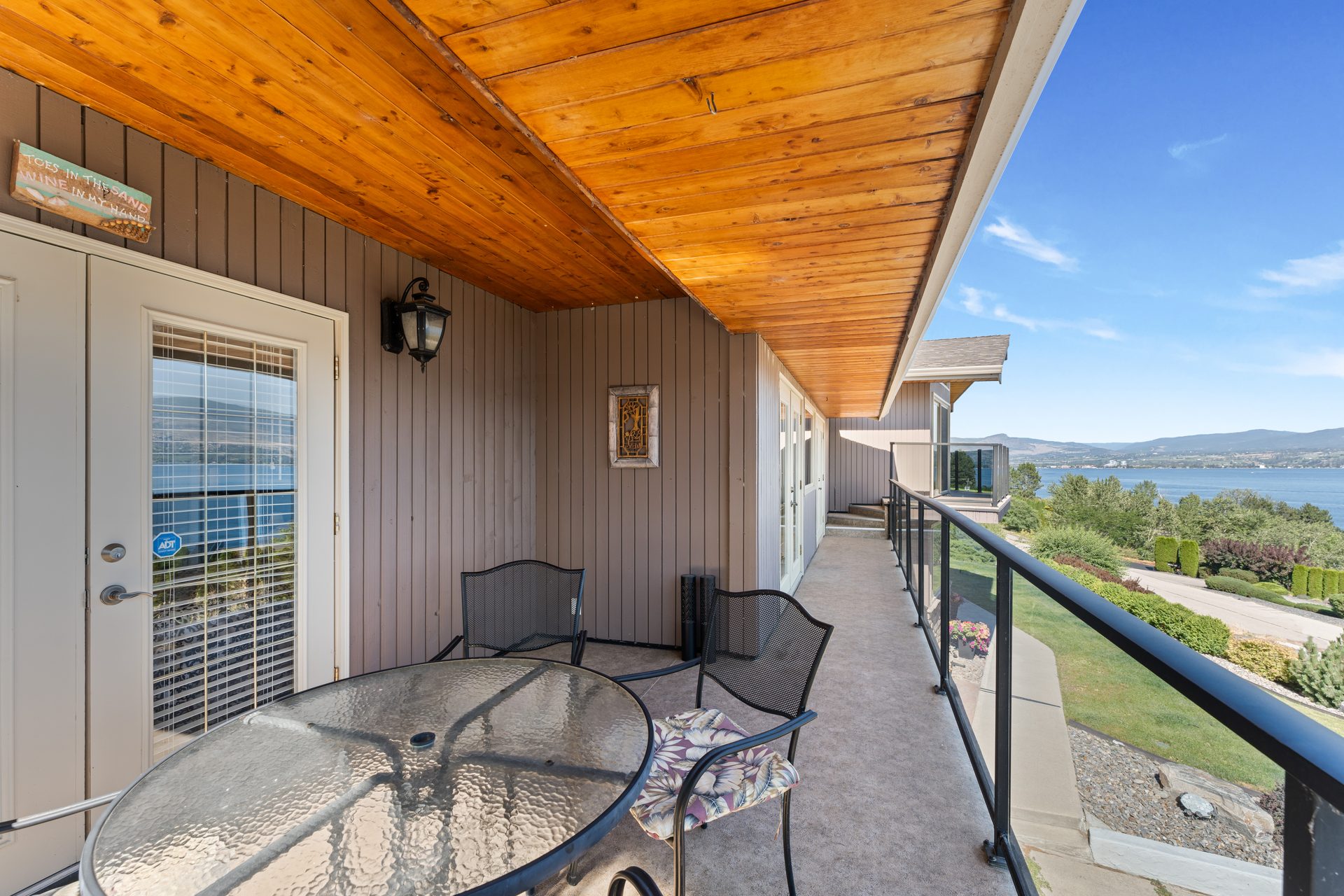 Covered front balcony with patio table, chairs and panoramic Okanagan Lake and mountain view