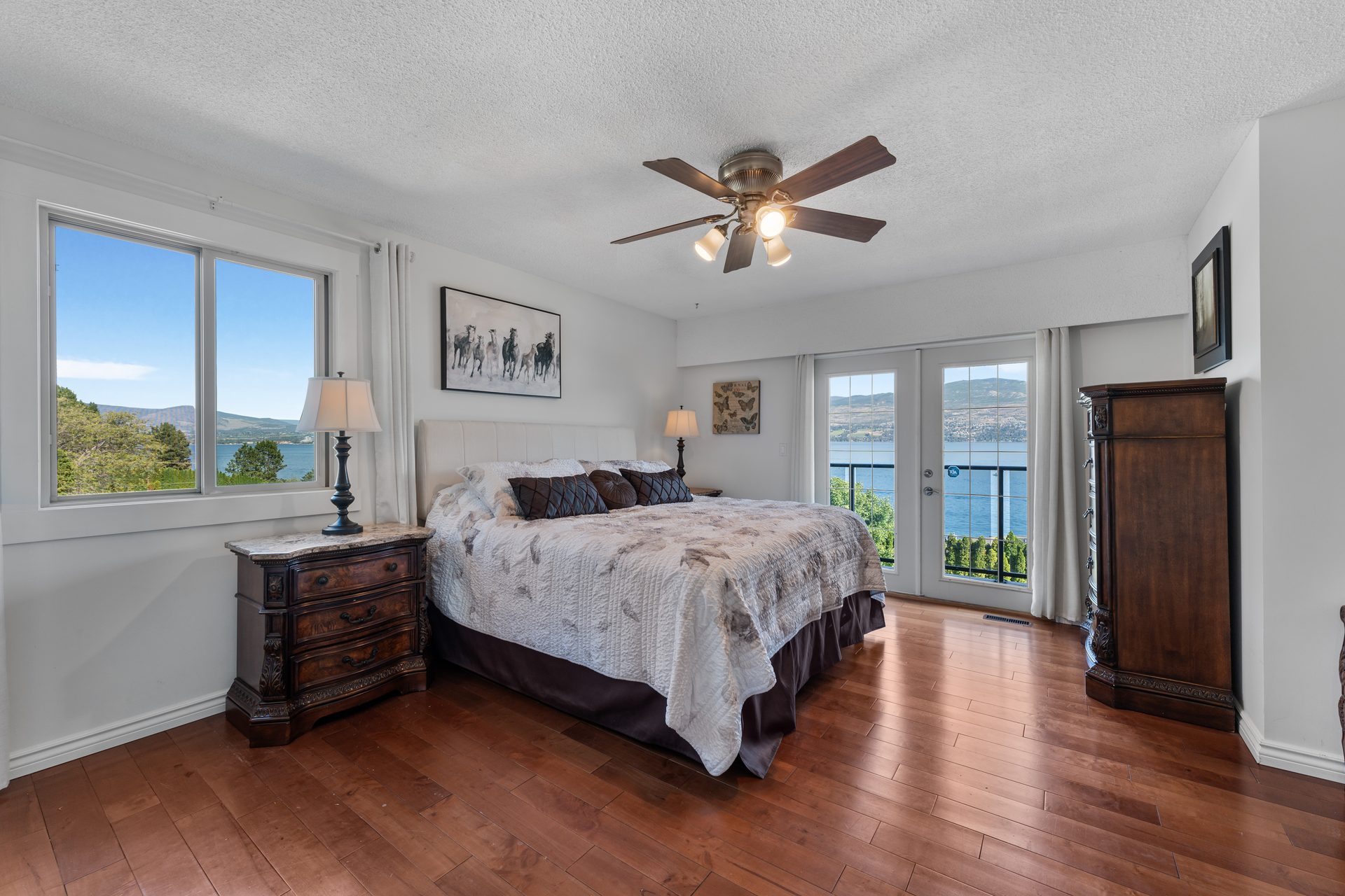Master bedroom with king bed, lake view through French doors, ceiling fan and dark wood furnishings