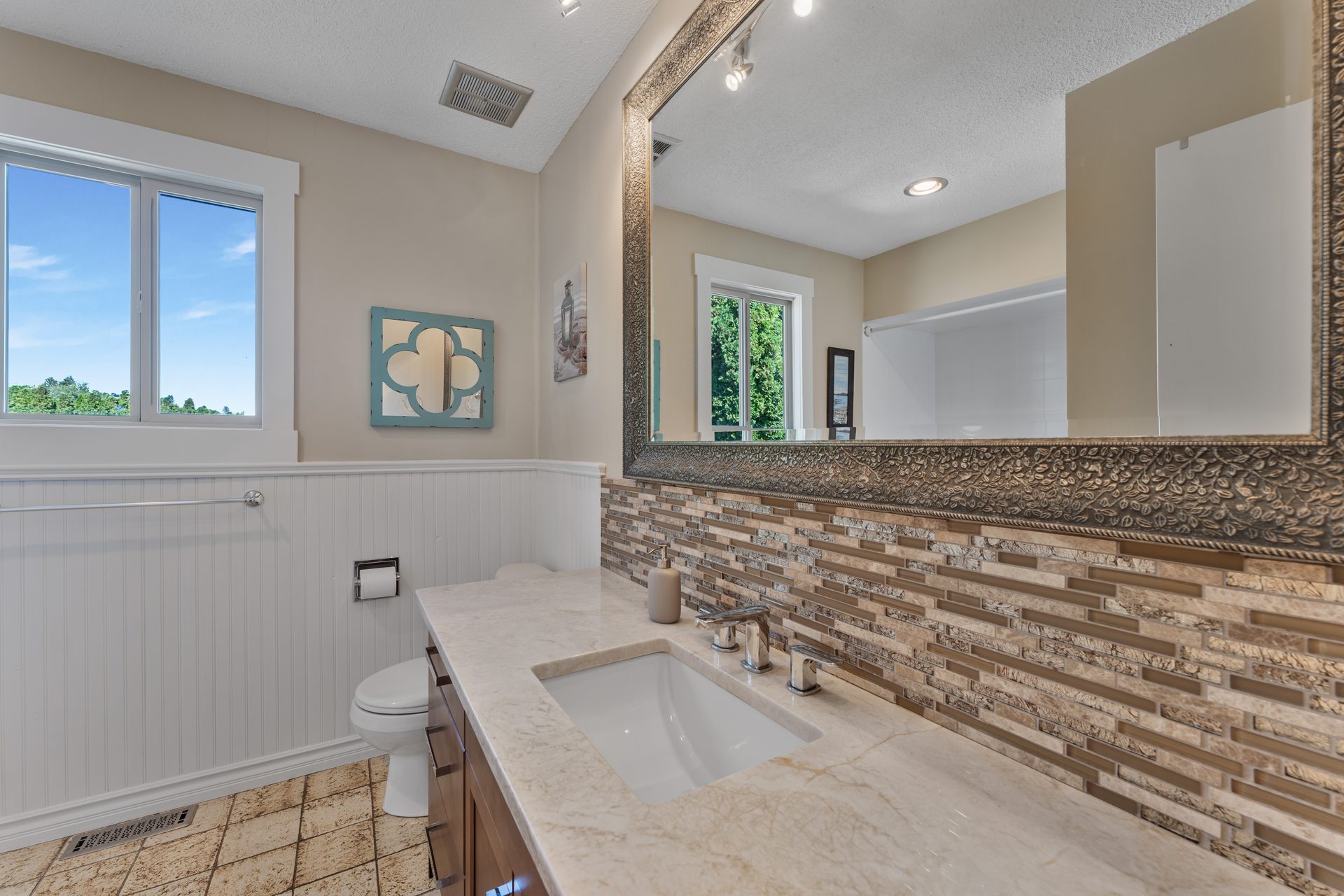 Main bathroom with marble vanity, mosaic tile backsplash and framed mirror