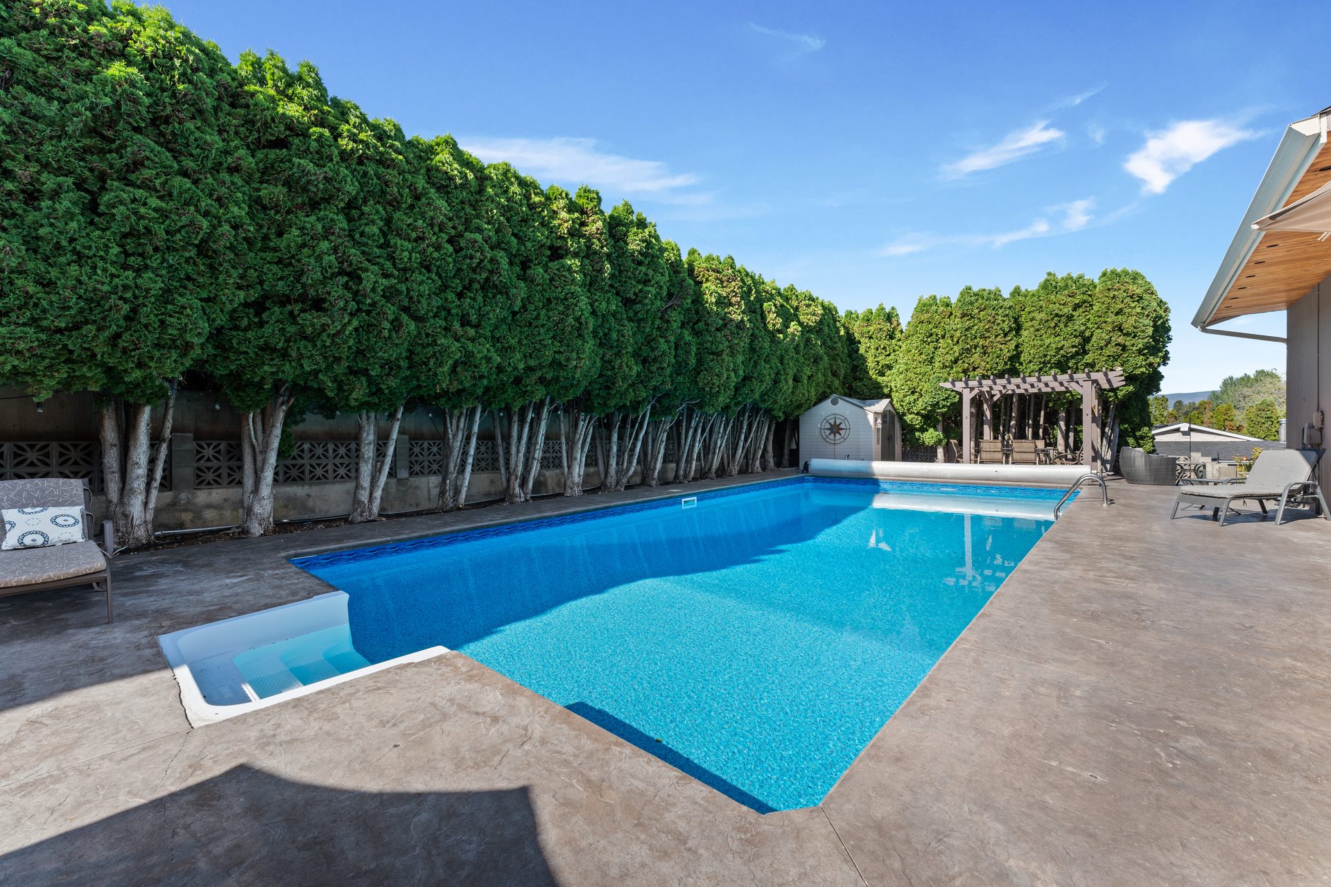 Private heated pool with cedar hedge privacy screen, lounge chairs and pergola